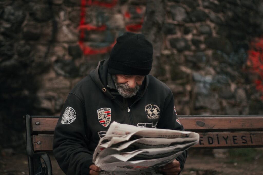 An elderly man reading a newspaper on a wooden bench in İstanbul, Türkiye.